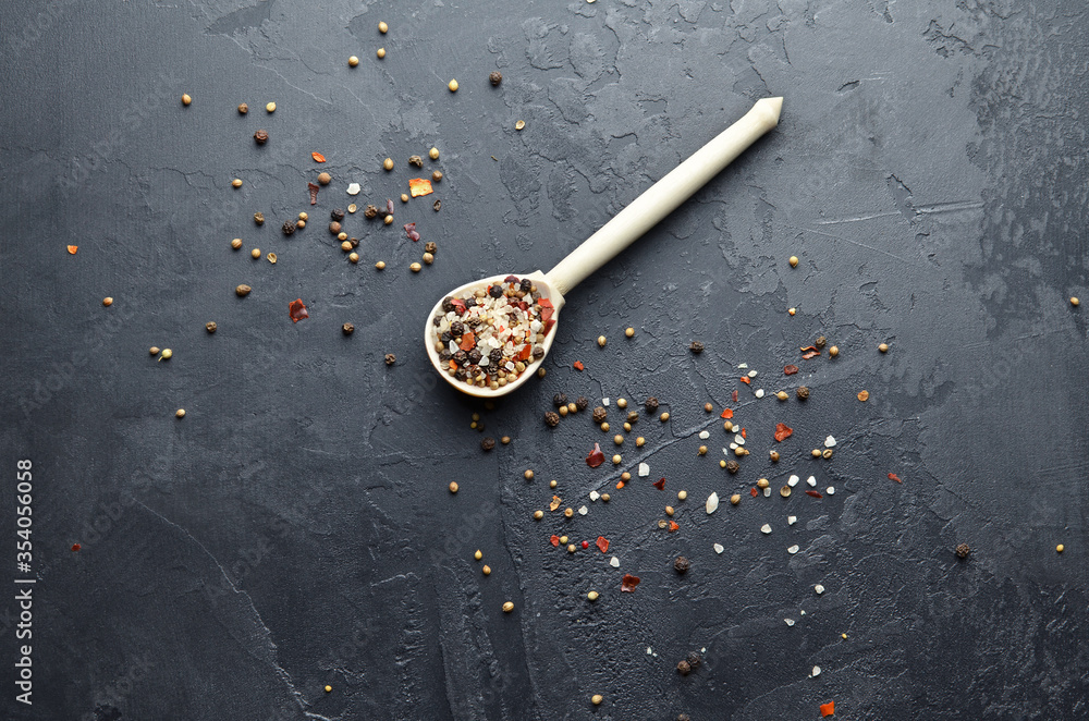 Sea salt, different peppers, cardamon, mustard seeds and paprika flakes in wooden spoon. Mixture of different kinds of spices on dark grunge background. Top view. Copy space. Sea salt, different peppers, cardamon, mustard seeds and paprika flakes in wooden spoon. Mixture of different kinds of spices on dark grunge background. Top view. Copy space.