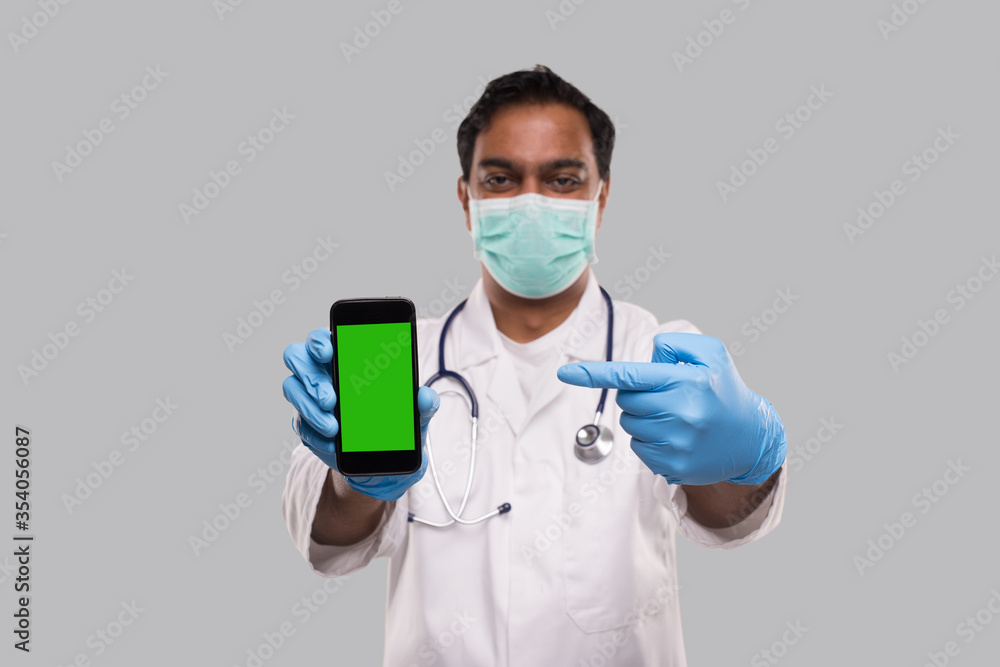 Doctor Pointing at Phone Wearing Medical Mask and Gloves. Indian Man Doctor Technology Medicine at Home. Phone Green Screen Isolated Doctor Pointing at Phone Wearing Medical Mask and Gloves. Indian Man Doctor Technology Medicine at Home. Phone Green Screen Isolated
