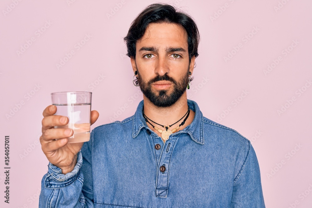 Young handsome hispanic bohemian hipster man with bear drinking a fresh glass of water with a confident expression on smart face thinking serious Young handsome hispanic bohemian hipster man with bear drinking a fresh glass of water with a confident expression on smart face thinking serious