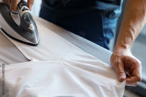 Man ironing white shirt, men's hands and iron, side view, cropped image, close up