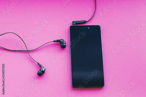 Smartphone and earphones on pink background