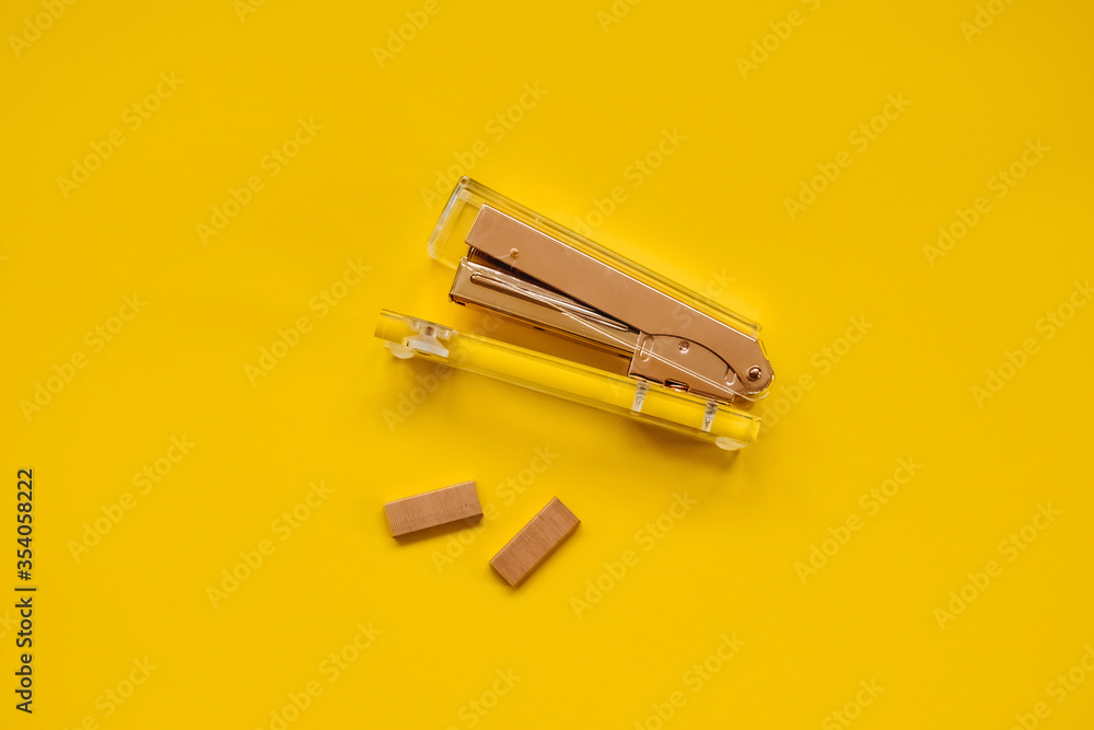 Stapler and staples made of pink golden metal and clear plastic on yellow background. Stapler and staples made of pink golden metal and clear plastic on yellow background.