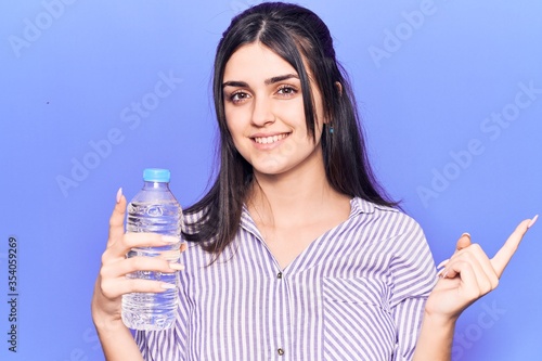 Young beautiful girl holding bottle of water smiling happy pointing with hand and finger to the side