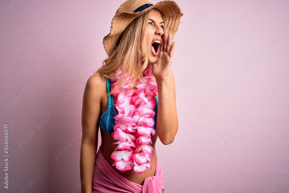 Young beautiful blonde woman on vacation wearing bikini and hat with hawaiian lei flowers shouting and screaming loud to side with hand on mouth. Communication concept. Young beautiful blonde woman on vacation wearing bikini and hat with hawaiian lei flowers shouting and screaming loud to side with hand on mouth. Communication concept.