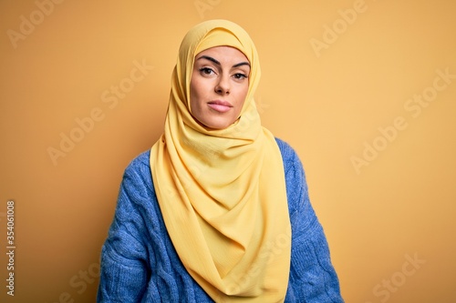Young beautiful brunette muslim woman wearing arab hijab over isolated yellow background looking sleepy and tired, exhausted for fatigue and hangover, lazy eyes in the morning. © Krakenimages.com