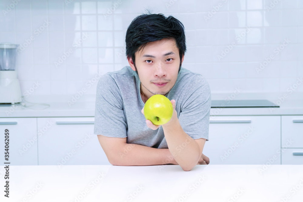 Attractive smiling young man holding green fresh apple breakfast in his kitchen looking camera. Handsome male showing green apple on table at home. Healthy food concept. Attractive smiling young man holding green fresh apple breakfast in his kitchen looking camera. Handsome male showing green apple on table at home. Healthy food concept.