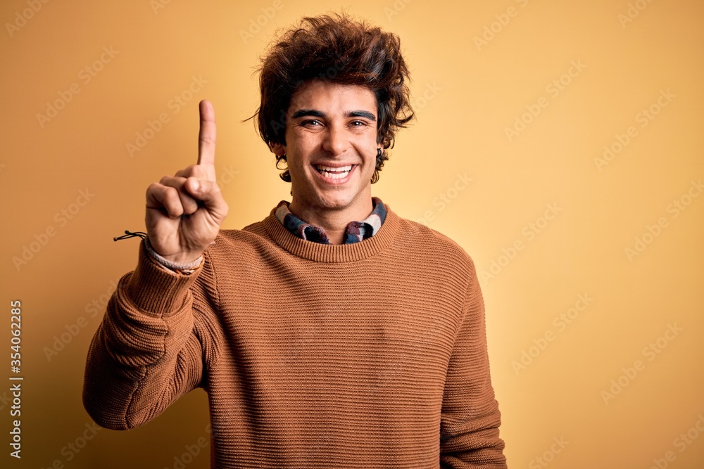 Young handsome man wearing casual shirt and sweater over isolated yellow background pointing finger up with successful idea. Exited and happy. Number one. Young handsome man wearing casual shirt and sweater over isolated yellow background pointing finger up with successful idea. Exited and happy. Number one.