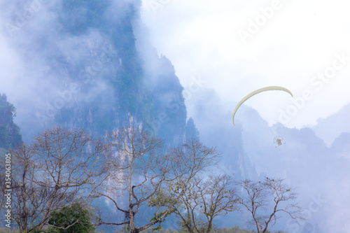 Landscape view of Paramotor isolated flying over the mountain view and misty in sky cloudy morning time