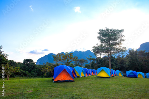 The Colorful Camping Tents on a glade and sunrise in the national park near the mountain in the morning light on blue sky cloud