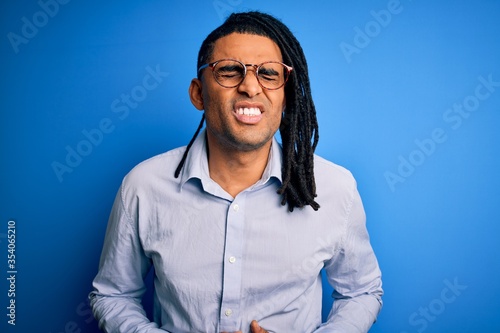 Young handsome african american man with dreadlocks wearing casual shirt and glasses with hand on stomach because indigestion, painful illness feeling unwell. Ache concept.