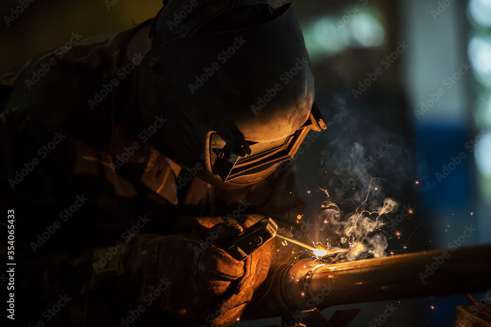 Welder at work. Man in a protective mask. The welder makes seams on the metal. Sparks and smoke when welding. Welder at work. Man in a protective mask. The welder makes seams on the metal. Sparks and smoke when welding.