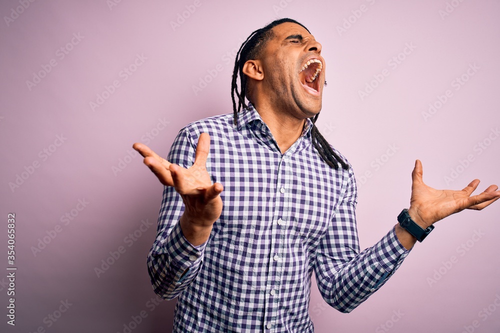 Fototapeta premium Young handsome african american afro man with dreadlocks wearing casual shirt celebrating mad and crazy for success with arms raised and closed eyes screaming excited. Winner concept
