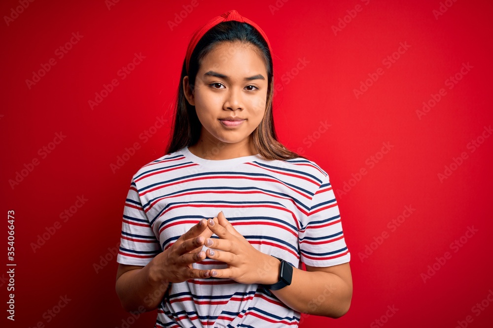 Young beautiful asian girl wearing casual striped t-shirt over isolated red background Hands together and fingers crossed smiling relaxed and cheerful. Success and optimistic Young beautiful asian girl wearing casual striped t-shirt over isolated red background Hands together and fingers crossed smiling relaxed and cheerful. Success and optimistic