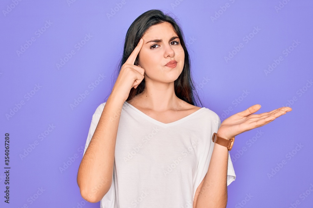 Young beautiful brunette woman wearing casual white t-shirt over purple background confused and annoyed with open palm showing copy space and pointing finger to forehead. Think about it. Young beautiful brunette woman wearing casual white t-shirt over purple background confused and annoyed with open palm showing copy space and pointing finger to forehead. Think about it.