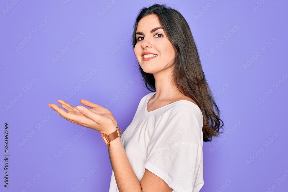 Young beautiful brunette woman wearing casual white t-shirt over purple background pointing aside with hands open palms showing copy space, presenting advertisement smiling excited happy Young beautiful brunette woman wearing casual white t-shirt over purple background pointing aside with hands open palms showing copy space, presenting advertisement smiling excited happy