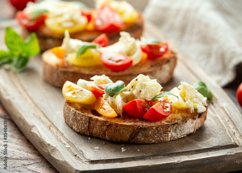 Tomato bruschetta and mozzarella cheese with basil on a rustic wooden board Tomato bruschetta and mozzarella cheese with basil on a rustic wooden board