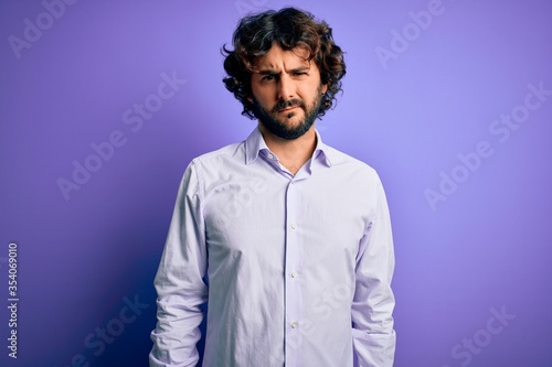 Young handsome business man with beard wearing shirt standing over purple background skeptic and nervous, frowning upset because of problem. Negative person.