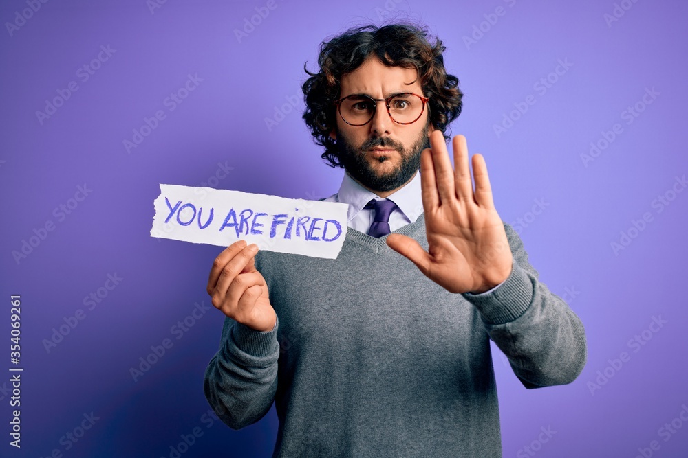 Handsome business man with beard holding you are fired message over purple background with open hand doing stop sign with serious and confident expression, defense gesture Handsome business man with beard holding you are fired message over purple background with open hand doing stop sign with serious and confident expression, defense gesture