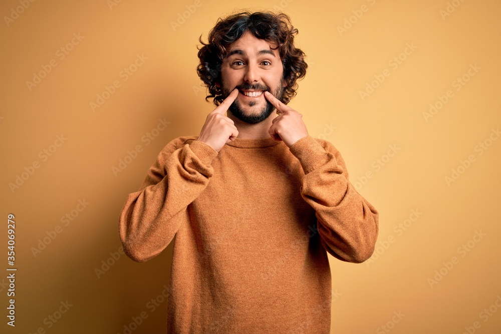 Young handsome man with beard wearing casual sweater standing over yellow background Smiling with open mouth, fingers pointing and forcing cheerful smile Young handsome man with beard wearing casual sweater standing over yellow background Smiling with open mouth, fingers pointing and forcing cheerful smile
