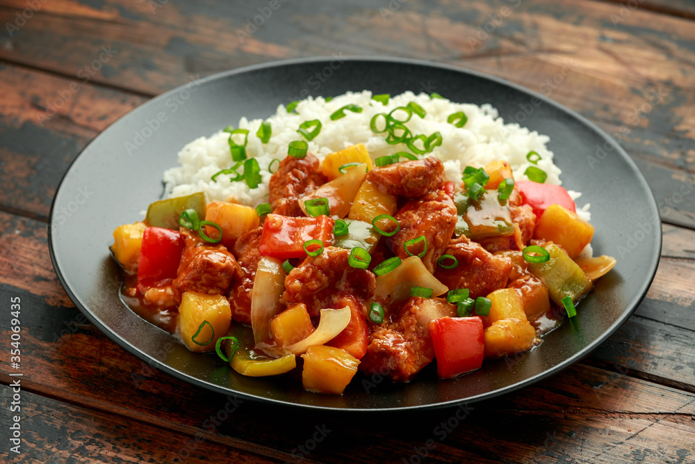 Pineapple and Chicken in sweet and sour sauce with bell pepper, rice and spring onion in black plate Pineapple and Chicken in sweet and sour sauce with bell pepper, rice and spring onion in black plate