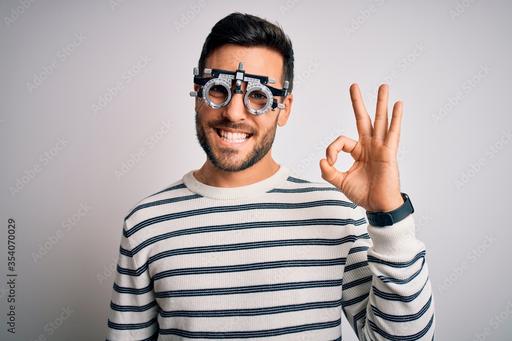 Young handsome man with beard wearing optometry glasses over isolated white background smiling positive doing ok sign with hand and fingers. Successful expression. Young handsome man with beard wearing optometry glasses over isolated white background smiling positive doing ok sign with hand and fingers. Successful expression.