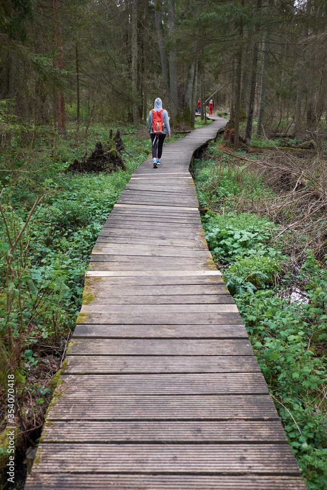 Fototapeta premium Travel. Young girl traveler with orange backpack and children has a walk on a wooden bridge in nature reserve.