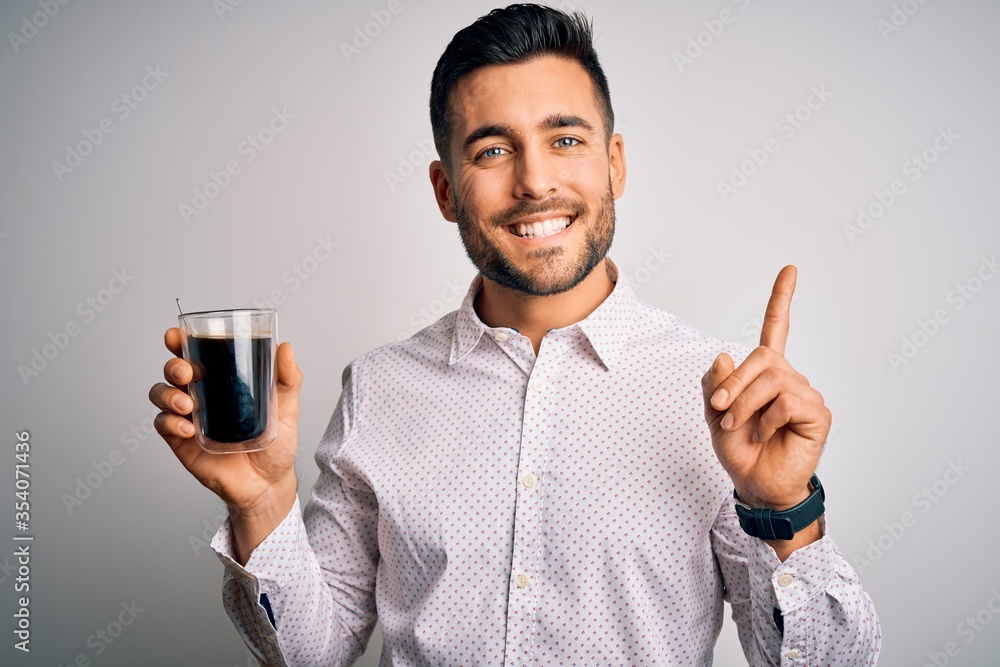 Young handsome man drinking a cup of hot coffee over white isolated background surprised with an idea or question pointing finger with happy face, number one Young handsome man drinking a cup of hot coffee over white isolated background surprised with an idea or question pointing finger with happy face, number one
