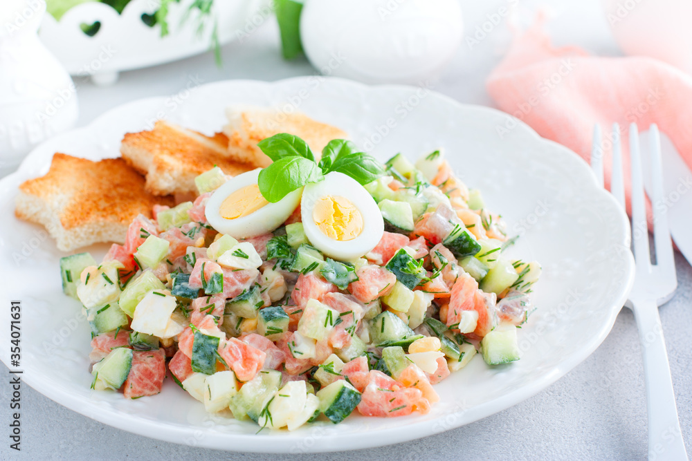 Salad with red fish, fresh cucumbers and herbs, an egg on a white plate with white bread toasts, selective focus Salad with red fish, fresh cucumbers and herbs, an egg on a white plate with white bread toasts, selective focus