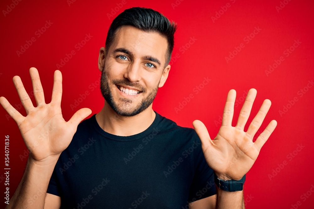Naklejka premium Young handsome man wearing casual black t-shirt standing over isolated red background showing and pointing up with fingers number ten while smiling confident and happy.
