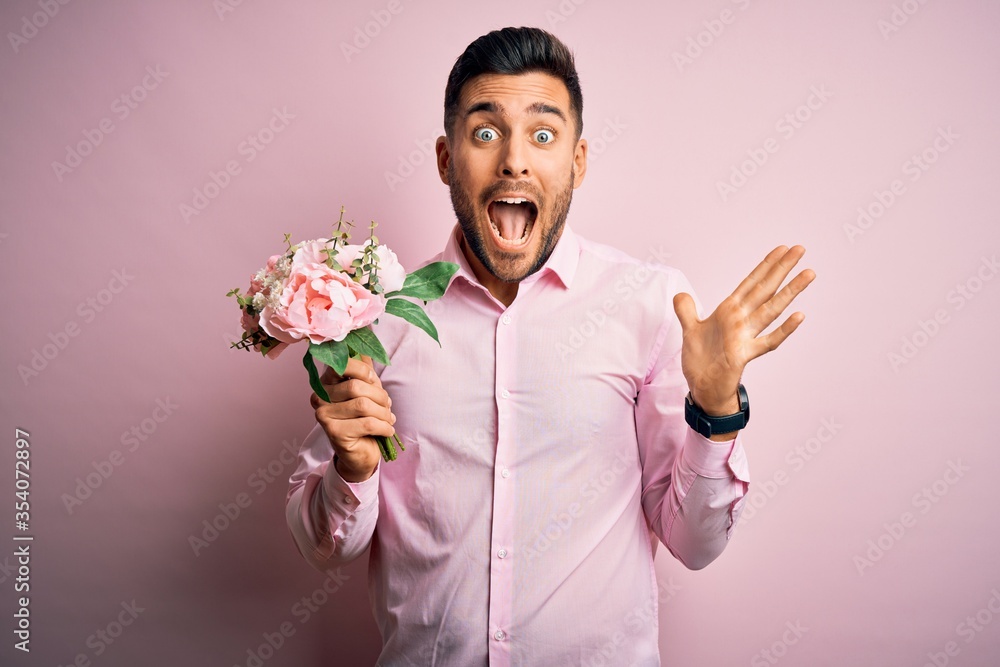 Young romatic man holding bouquet of spring flowers over pink isolatd background very happy and excited, winner expression celebrating victory screaming with big smile and raised hands Young romatic man holding bouquet of spring flowers over pink isolatd background very happy and excited, winner expression celebrating victory screaming with big smile and raised hands