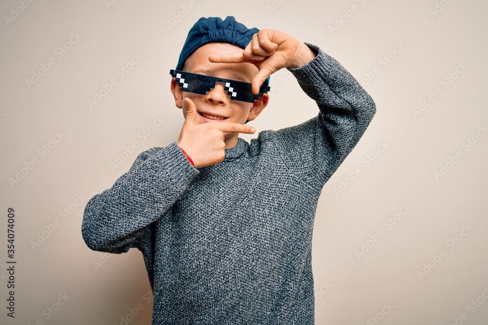 Young little caucasian kid wearing internet meme thug life glasses over isolated background smiling making frame with hands and fingers with happy face. Creativity and photography concept. Young little caucasian kid wearing internet meme thug life glasses over isolated background smiling making frame with hands and fingers with happy face. Creativity and photography concept.