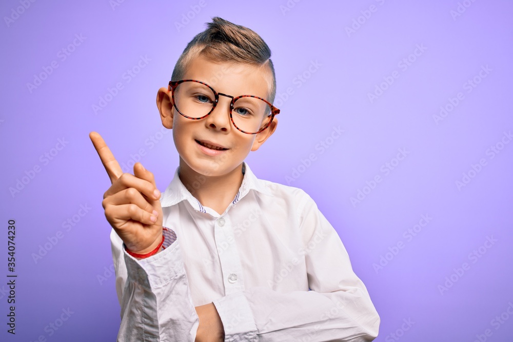 Young little caucasian kid with blue eyes wearing glasses and white shirt over purple background with a big smile on face, pointing with hand and finger to the side looking at the camera. Young little caucasian kid with blue eyes wearing glasses and white shirt over purple background with a big smile on face, pointing with hand and finger to the side looking at the camera.