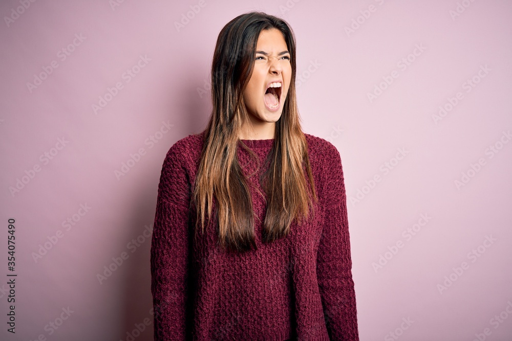Young beautiful girl wearing casual sweater over isolated pink background angry and mad screaming frustrated and furious, shouting with anger. Rage and aggressive concept. Young beautiful girl wearing casual sweater over isolated pink background angry and mad screaming frustrated and furious, shouting with anger. Rage and aggressive concept.
