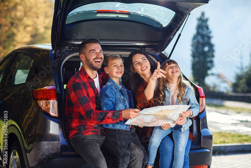 Photography Satisfied family of handsome father, pretty mother and lovely kids which are looking on the road map while sitting in the car's trunk at joint family vacation