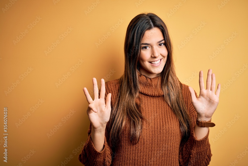 Young beautiful girl wearing casual sweater standing over isolated yellow background showing and pointing up with fingers number nine while smiling confident and happy. Young beautiful girl wearing casual sweater standing over isolated yellow background showing and pointing up with fingers number nine while smiling confident and happy.