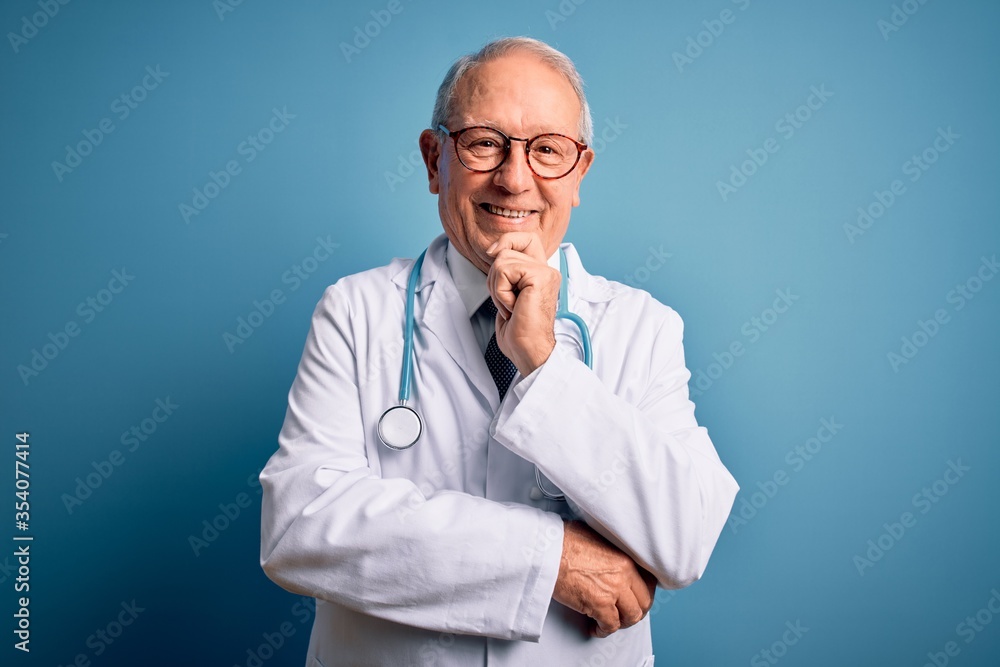 Senior grey haired doctor man wearing stethoscope and medical coat over blue background looking confident at the camera with smile with crossed arms and hand raised on chin. Thinking positive. Senior grey haired doctor man wearing stethoscope and medical coat over blue background looking confident at the camera with smile with crossed arms and hand raised on chin. Thinking positive.