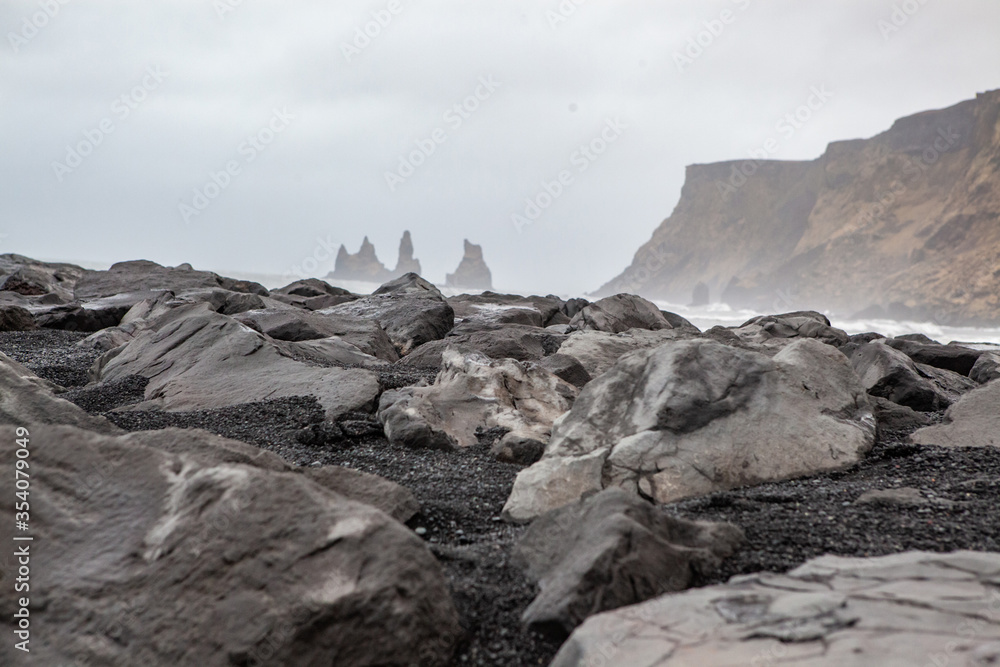 Black stones with large rock formations in the background in Iceland.Reynisfjara black sand beach in Iceland at winter. Famous Reynisdrangar rock formations at black Reynisfjara Beach.