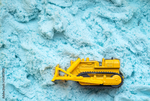 Toy yellow, cargo bulldozer on a blue background made of magnetic sand. Toy and industry.
