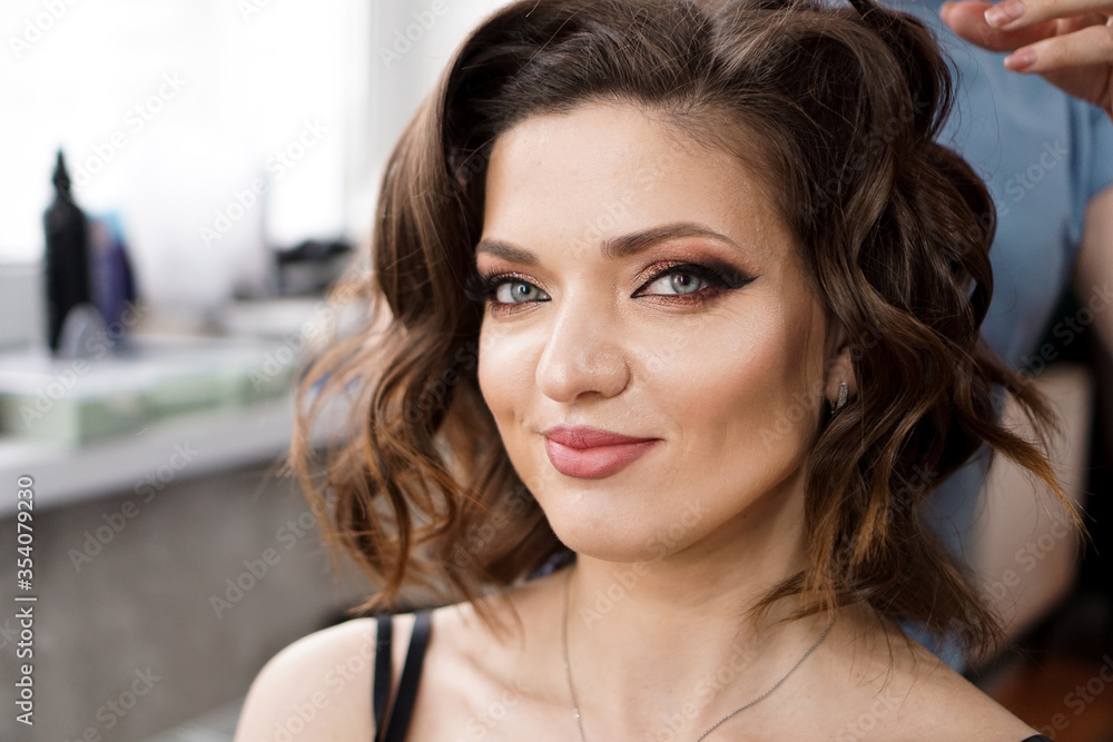 The hairdresser makes a hairstyle with curls to a beautiful brunette with medium long hair. Model is looking at the camera. The hairdresser makes a hairstyle with curls to a beautiful brunette with medium long hair. Model is looking at the camera.