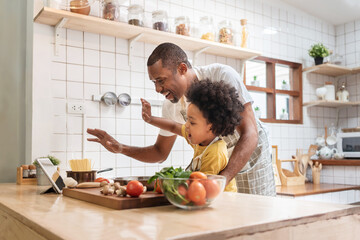 African Father and son make video call with digital tablet with family while cooking in kitchen