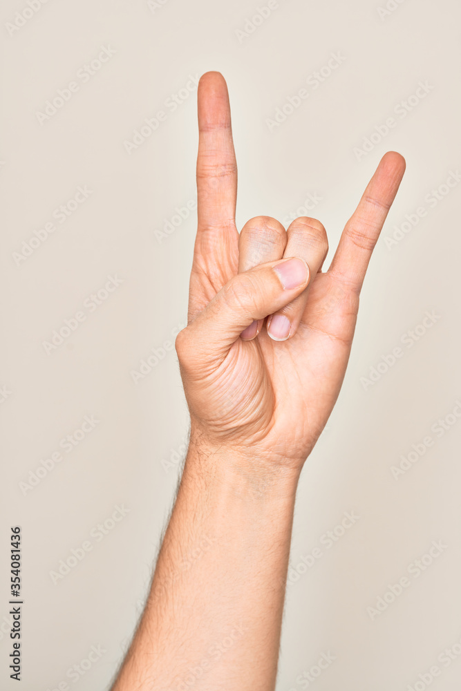 Hand of caucasian young man showing fingers over isolated white background gesturing rock and roll symbol, showing obscene horns gesture Hand of caucasian young man showing fingers over isolated white background gesturing rock and roll symbol, showing obscene horns gesture