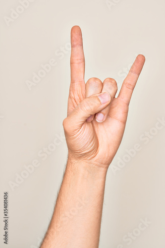 Hand of caucasian young man showing fingers over isolated white background gesturing rock and roll symbol  showing obscene horns gesture