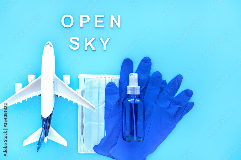 Fototapeta premium Travel after pandemic. Open sky after coronavirus. Plane, Blue passport with medical mask, Protective gloves, Bottle of Hand Sanitizer. Creative flat lay safety travel concept. With space for text.