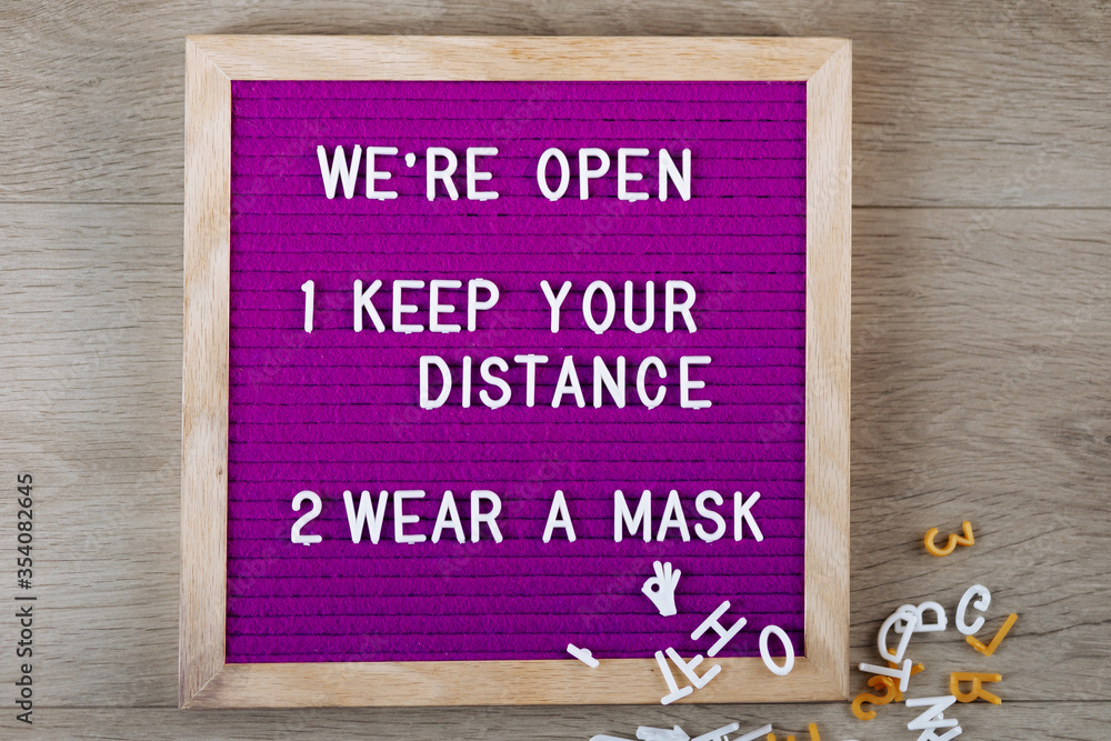 Obraz premium We're open, keep your distance, wear a mask text on purple letter board near the notebook. Business concept. Service, restaurant, shop and cafe. Reopening of the place after the quarantine covid-19.