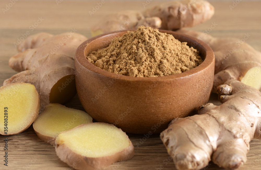 Ginger powder in a brown wooden bowl and fresh ginger root on a wooden background. Ginger powder in a brown wooden bowl and fresh ginger root on a wooden background.