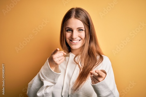 Young beautiful redhead sporty woman wearing sweatshirt over isolated yellow background pointing fingers to camera with happy and funny face. Good energy and vibes. © Krakenimages.com