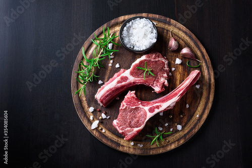 Two raw lamb chops on a wooden cutting board with spices on a dark wooden background photo