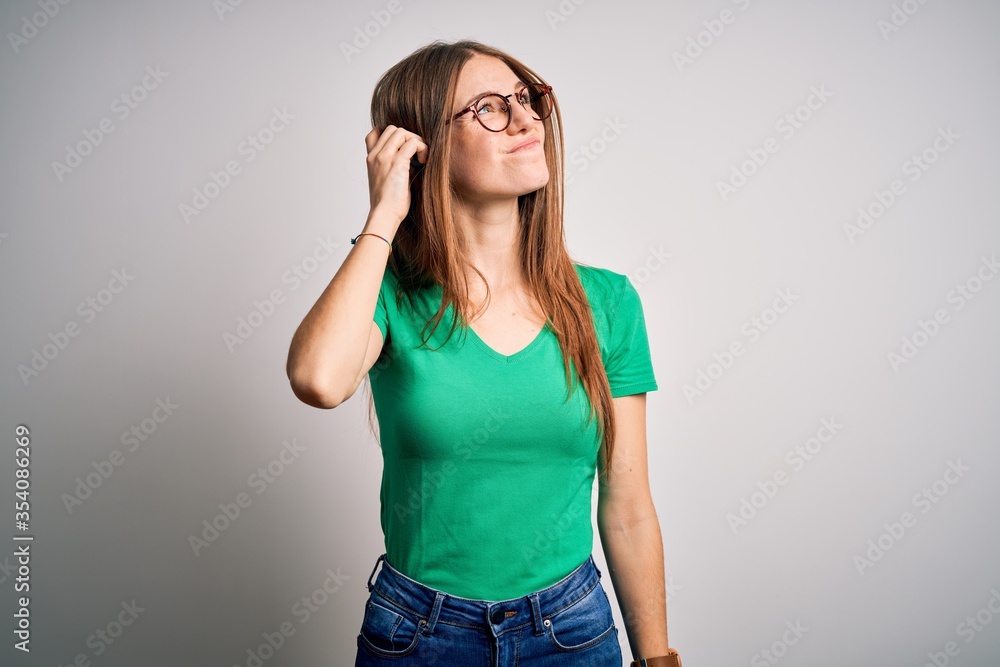 Young beautiful redhead woman wearing casual green t-shirt and glasses over white background confuse and wondering about question. Uncertain with doubt, thinking with hand on head. Pensive concept. Young beautiful redhead woman wearing casual green t-shirt and glasses over white background confuse and wondering about question. Uncertain with doubt, thinking with hand on head. Pensive concept.