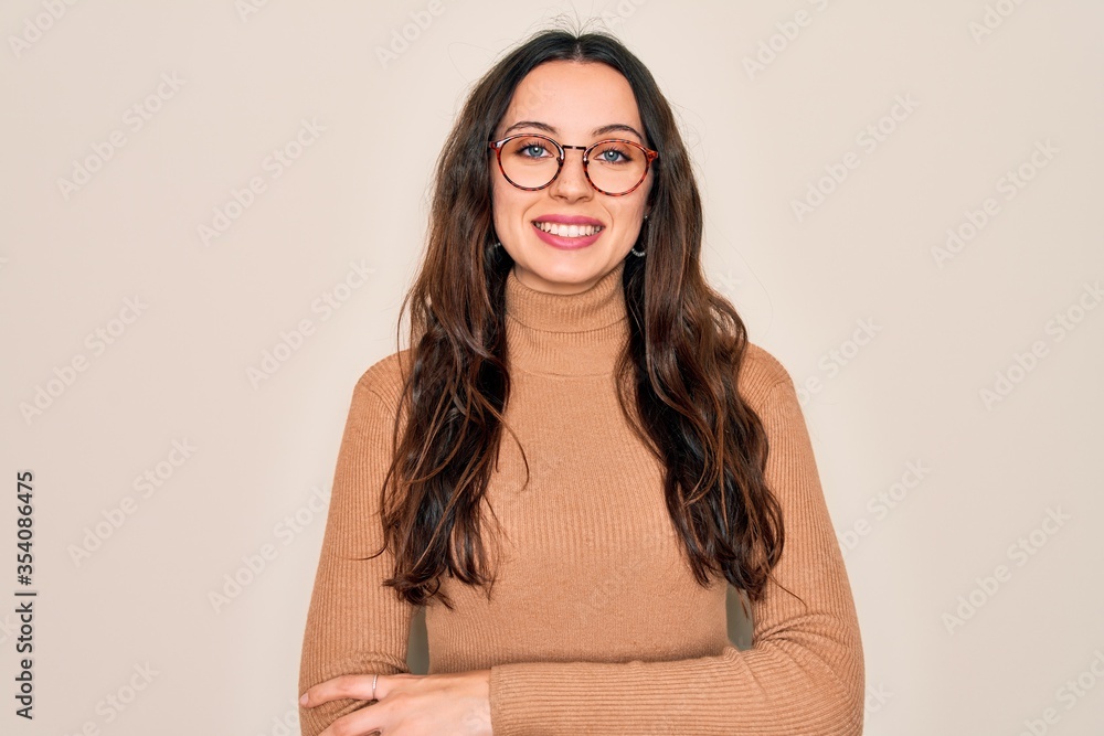 Young beautiful woman wearing casual turtleneck sweater and glasses over white background happy face smiling with crossed arms looking at the camera. Positive person. Young beautiful woman wearing casual turtleneck sweater and glasses over white background happy face smiling with crossed arms looking at the camera. Positive person.