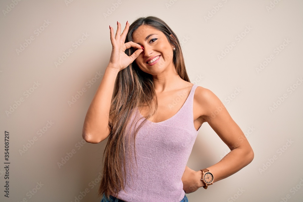 Young beautiful brunette woman with long hair standing over isolated background doing ok gesture with hand smiling, eye looking through fingers with happy face. Young beautiful brunette woman with long hair standing over isolated background doing ok gesture with hand smiling, eye looking through fingers with happy face.
